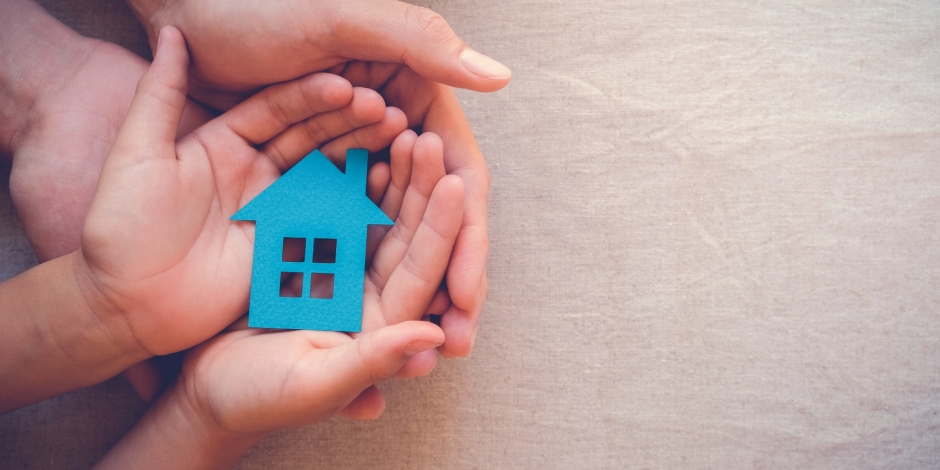 Adult and child's hands cupped holding a cutout of a house